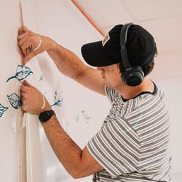 A laser guide projects a straight line, helping the installer align and position a vinyl panel with accuracy for a seamless wall mural.